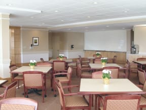 a dining room with tables and chairs and flowers in vases at McCormack House at Forest Park Southeast Senior apartments in St.  Louis, MO