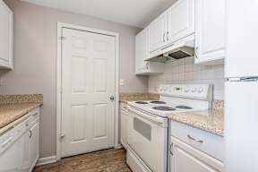 A white door is in a kitchen with white cabinets and a white stove.