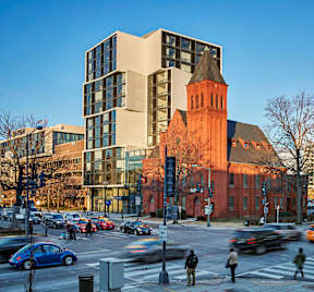 A busy street with cars and pedestrians in front of a church and a modern building.