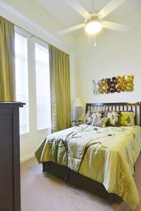 A bedroom with a bed, a ceiling fan, and a window with green curtains.