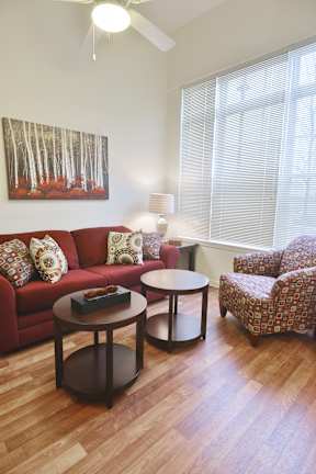 A living room with a red couch, a round table, and a painting on the wall.