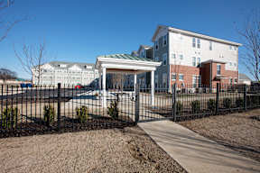 A white building with a green roof is behind a black fence.