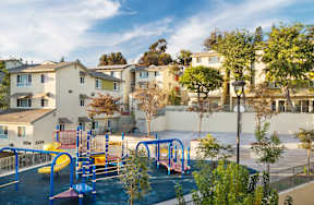 A playground with a blue slide and a yellow slide in front of apartment buildings.