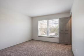 A room with a carpeted floor and a window with blinds.