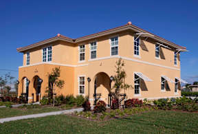 A yellow house with a red roof and a green lawn in front.