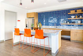 A kitchen with a white counter top and orange chairs.