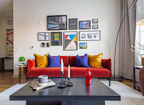 A living room with a red couch, a black coffee table, and a wall with framed pictures.