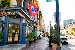 A street view of a city with a blue building on the left and a red flag hanging from a pole.