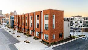 A row of red brick apartment buildings are lined up on a street.