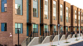 A long brick building with many windows and a black iron fence.