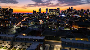 A cityscape at dusk with buildings illuminated and a clear sky.