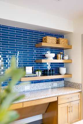 A kitchen with a blue tiled backsplash and wooden shelves.