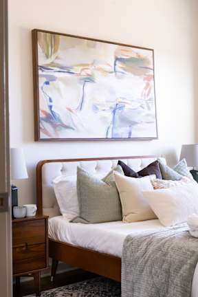 A bedroom with a bed, pillows, a nightstand, and a painting on the wall.