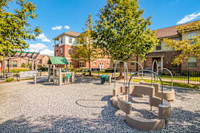 A playground with a swing set and a slide in the foreground and apartment buildings in the background.