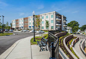 A street view of a residential area with apartment buildings and a bench.