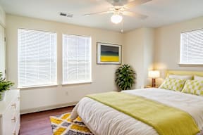 A bedroom with a bed, a ceiling fan, and a painting on the wall.