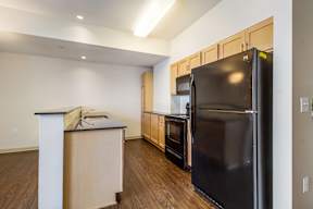 A black refrigerator is in a kitchen with wooden cabinets.