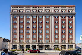 A red car is parked in front of a large building.