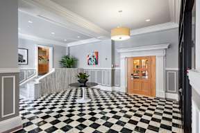 A black and white checkered floor in a foyer with a plant and a painting on the wall.