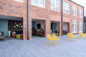 a patio with yellow chairs in front of a brick building
