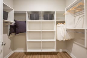 a walk in closet with white shelving and pillows