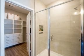 a walk in shower with a glass door and a closet with white shelves
