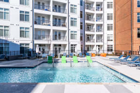 a swimming pool with green chairs in front of an apartment building