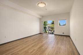 A room with wooden flooring and a window overlooking a balcony.