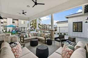 A patio with a white ceiling and a fan, furnished with a couch, chairs, and ottomans.
