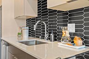 a kitchen counter with a sink and black tile walls at Hue Apartments, Redmond , Washington