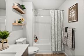 A bathroom with a white toilet, a white sink, a shower with a grey curtain, and a brown picture on the wall.