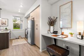 A modern kitchen with a refrigerator, a dining table with a bench, and a window.