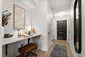 A white desk with a brown stool and a framed picture on the wall.
