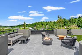 a rooftop patio with couches and tables and a fire pit at Hue Apartments, Redmond , WA 98052