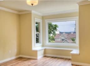 A room with a window seat and a view of houses across the street.