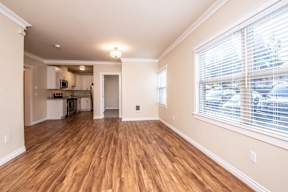 A room with wooden floors and a kitchen in the background.