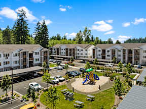 A playground with a slide is surrounded by a parking lot and apartment buildings.