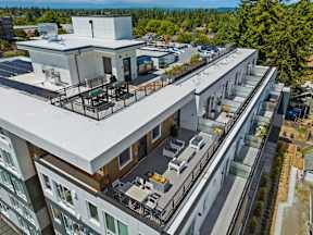 A modern building with a flat roof and balconies overlooks a parking lot and trees.