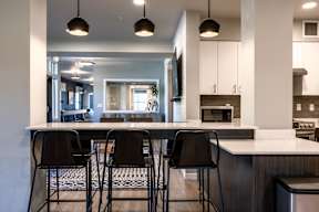 A modern kitchen with a bar area and four black chairs.