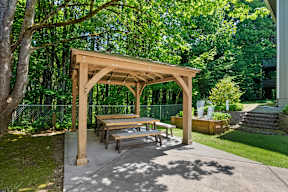 a picnic table under a wooden pavilion in a backyard