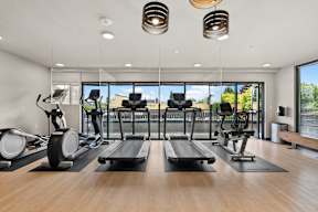 a gym with treadmills and other exercise equipment on a wooden floor and windows