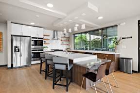 a kitchen with a large island with a white counter top and a stainless steel refrigerator