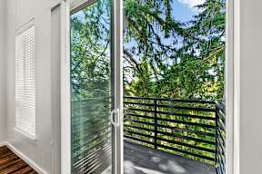 A glass door with a handle is open to a balcony with a black railing.