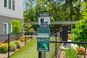 A sign for a dog waste station is posted on a fence.