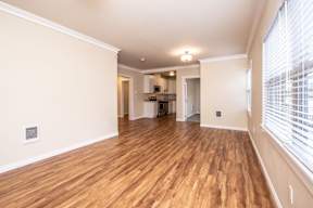 A room with wooden floors and a kitchen area in the background.