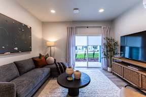 A living room with a grey couch, a black coffee table, and a large window with curtains.