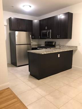 A kitchen with black cabinets and a stainless steel refrigerator.
