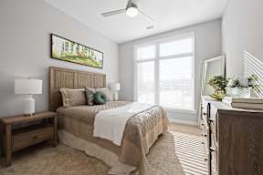 A carpeted bedroom with ample natural light from a large window and a ceiling fan.