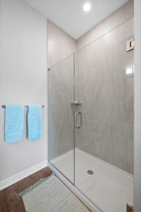 A stand-up shower with a frameless door and modern tile walls in a bathroom with hardwood-style flooring.