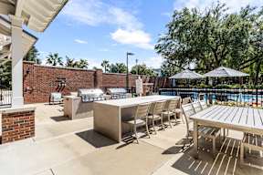 Outdoor grilling and dining area with bar seating and poolside umbrellas at The Flats at Tioga Town Center.